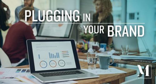 Table filled with laptops, charts, graphs, drinks and text: "Plugging in Your Brand."